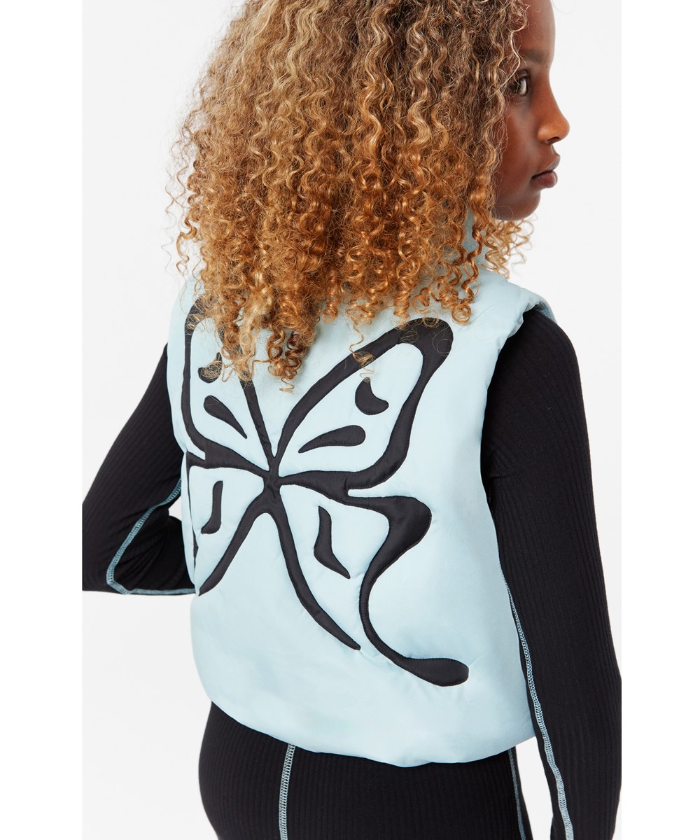 Hester - Quilt Butterfly - Lichtblauw doorgestikt vest voor kinderen van gerecycled polyester met een geborduurde zwarte vlinder op de achterkant.