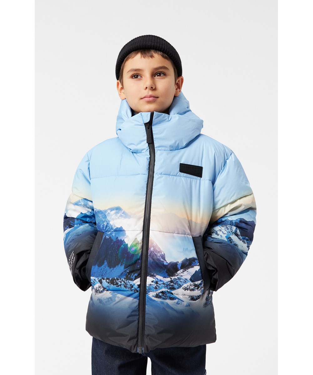 Hilo - High In Sky - Warme gewatteerde jas voor kinderen van gerecycled polyester met een print van de besneeuwde Alpen met zonnestralen en een helderblauwe lucht.