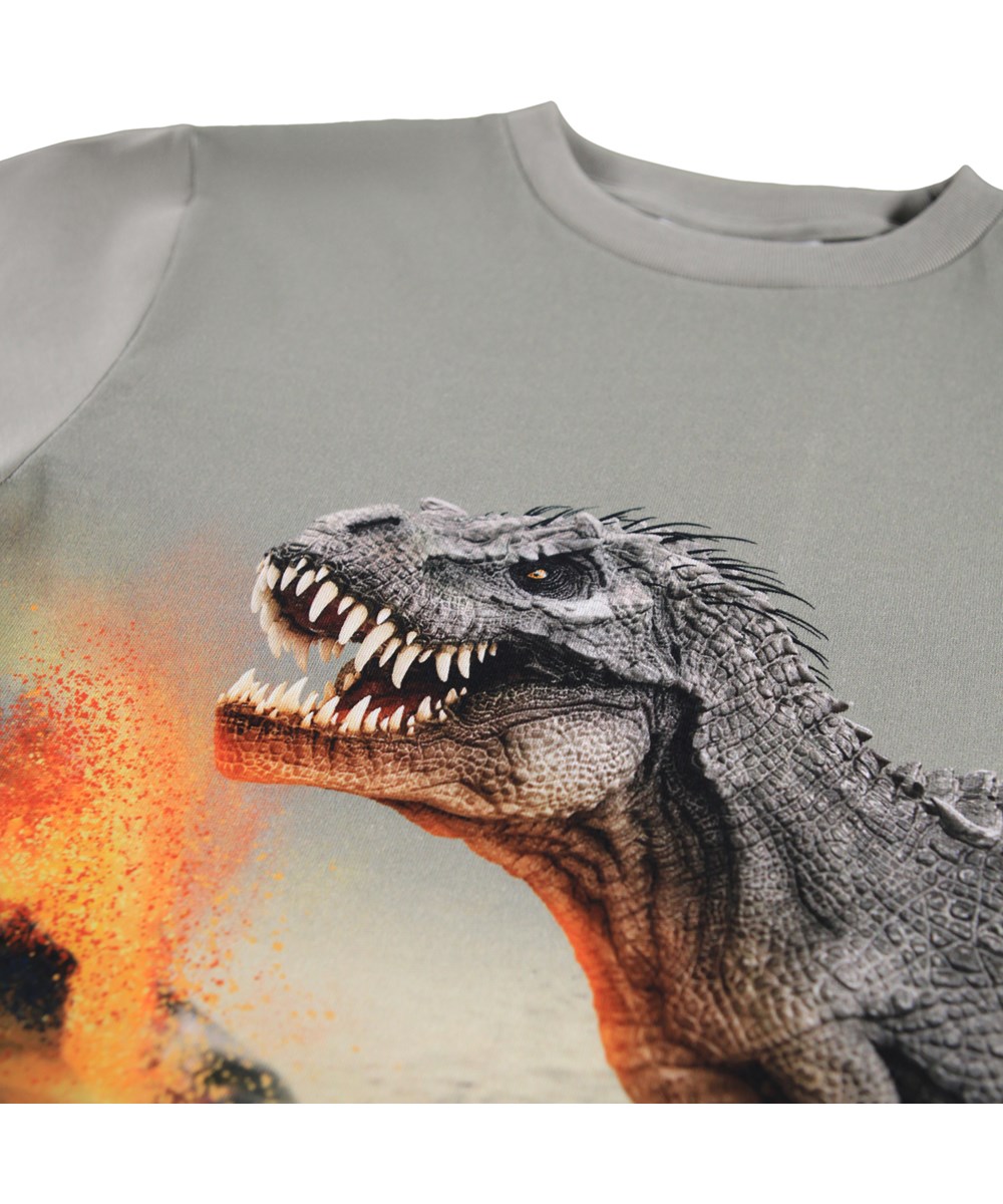Rube - Dinosaur Fog - Kakifarvet, langærmet bluse til børn i økologisk bomuld med ribkant i hals og et print af en tyrannosaurus og en vulkan i udbrud.