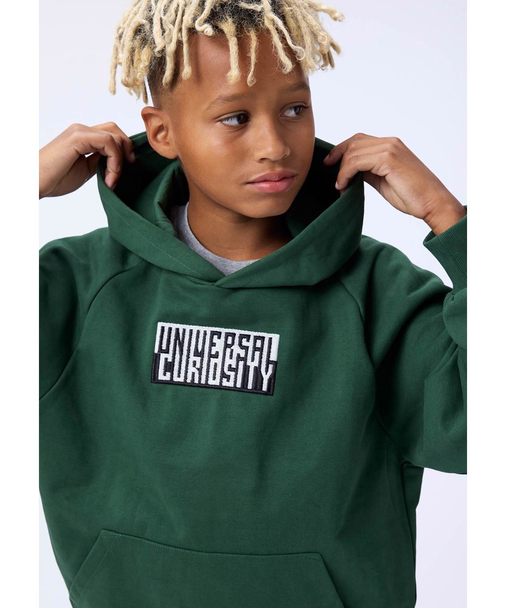 Mic - Pine Tree - Grøn hættetrøje til børn i økologisk bomuld med sort/hvid print med teksten ''Universal Curiosity''. 