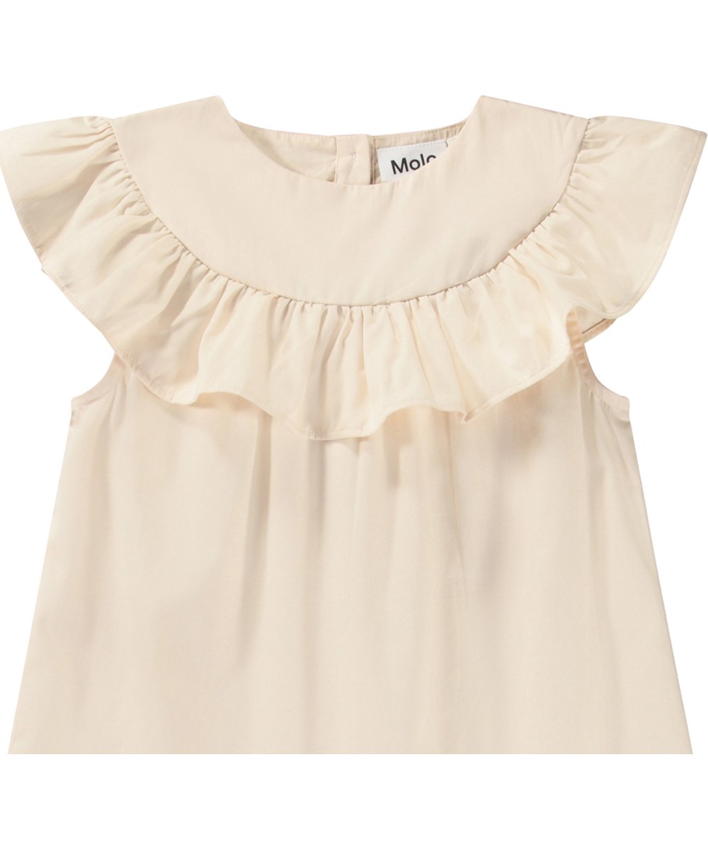 Celia - Brazilian Sand - Knälång beige A-linjeformad klänning med volangdetalj på axlarna och knappknäppning i nacken.