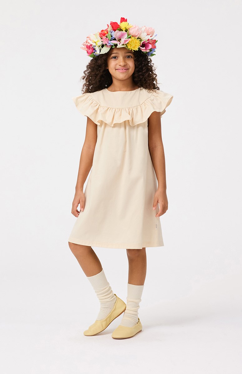 Celia - Brazilian Sand - Knälång beige A-linjeformad klänning med volangdetalj på axlarna och knappknäppning i nacken.