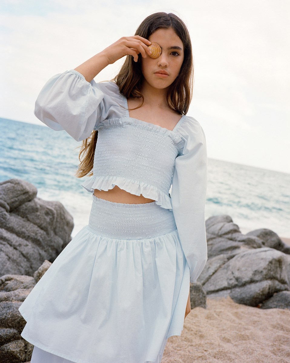 Rosemary - Skywriting - Light blue long-sleeved cropped blouse for children in soft cotton, with a smocked effect.