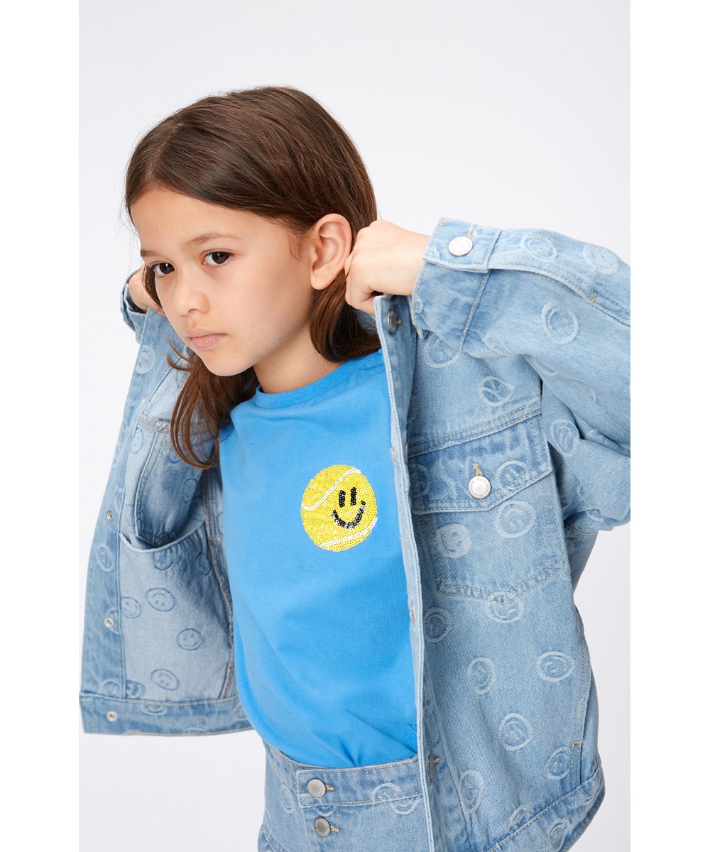 Ranva - Tennis Smile - Short sleeve, blue t-shirt in organic cotton with a sequined embroidery of a smiling, yellow tennis ball on the chest. 