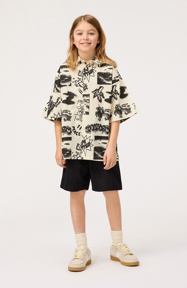 Richie - Art Mix - Beiges Shirt mit Aufdruck für Kinder aus weicher Öko-Baumwolle mit weiten T-Shirt-Ärmeln, klassischem Hemdkragen und Knopfverschluss auf der Vorderseite.