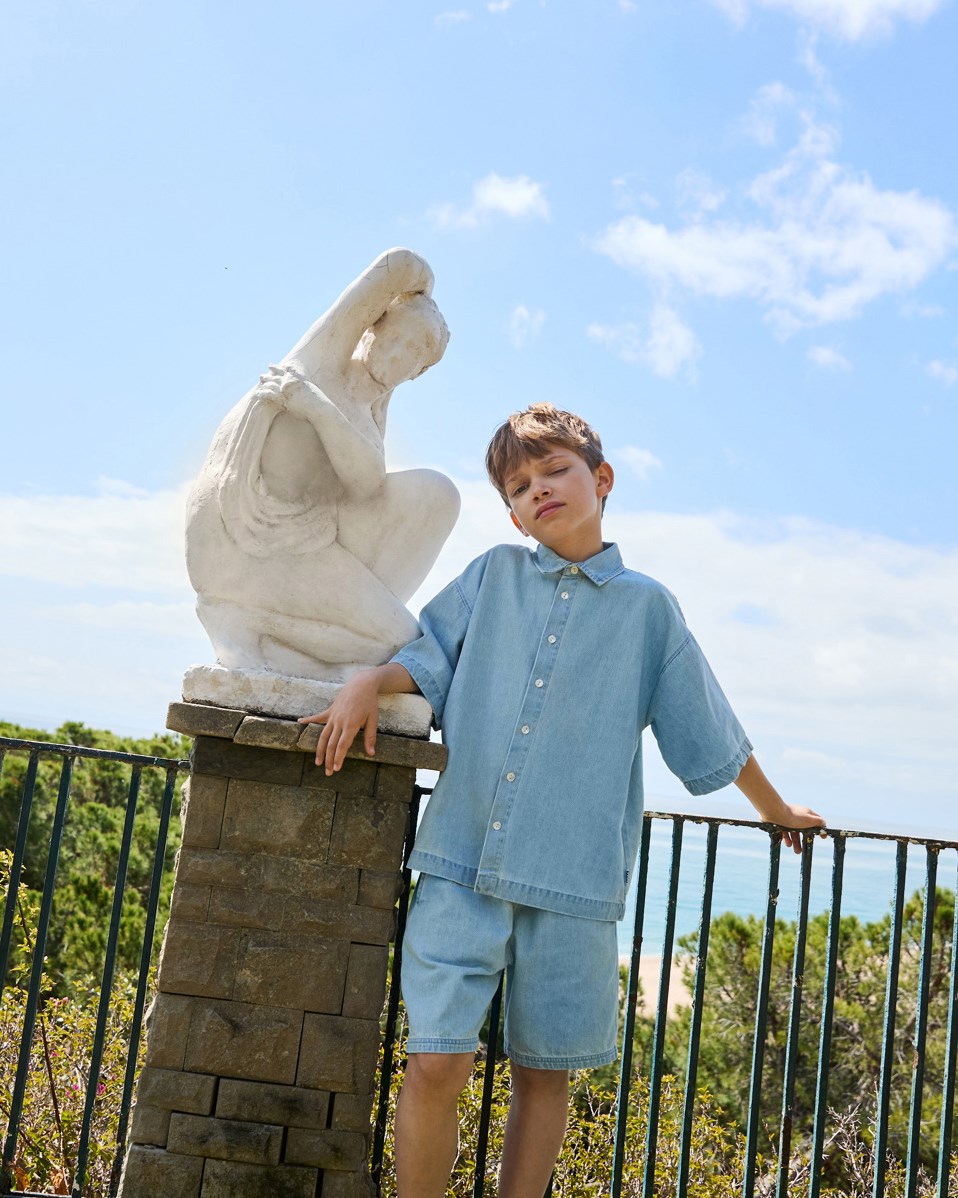 Richie - Misty Denim - Hellblaues Jeanshemd mit Druck für Kinder aus weicher Öko-Baumwolle mit weiten T-Shirt-Ärmeln, klassischem Hemdkragen und Knopfverschluss auf der Vorderseite.