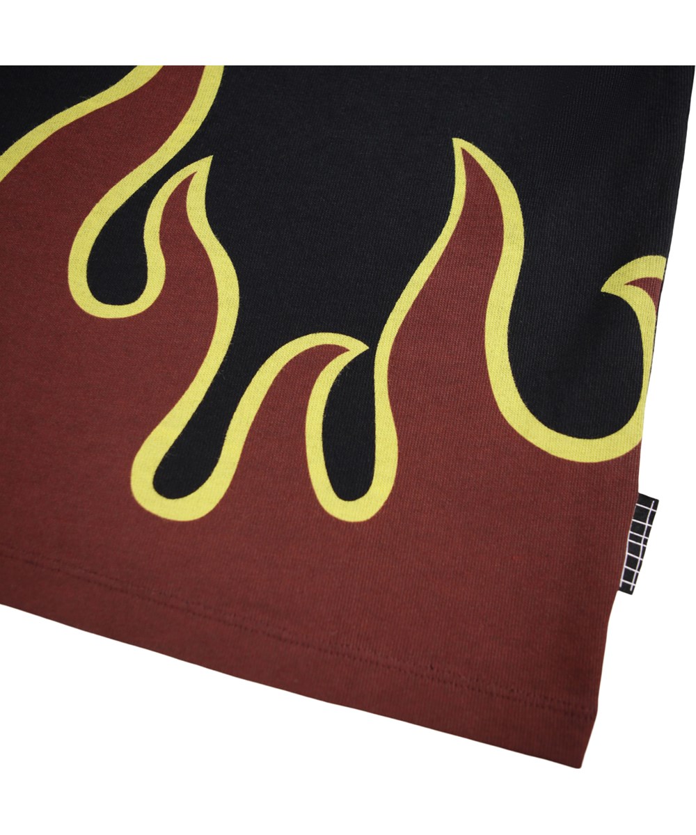 Riley - Hot - Schwarzes T-Shirt für Kinder aus weicher Öko-Baumwolle mit kurzen Ärmeln, einem gerippten Ausschnitt und einem Flammenmuster in Burgunderrot und Gelb am Saum.