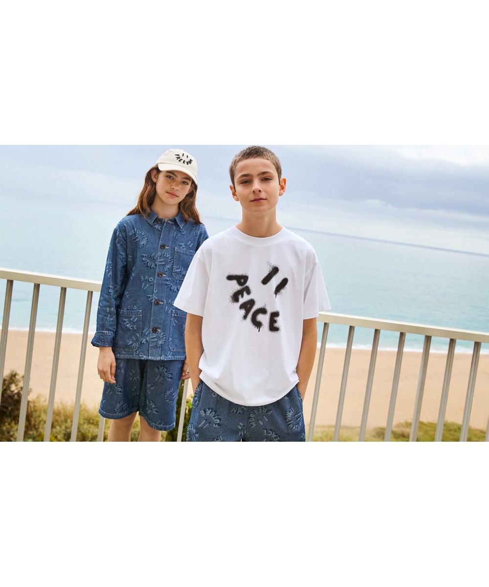 Riley - Peace Smile - Weißes T-Shirt mit Aufdruck für Kinder aus weicher Öko-Baumwolle mit kurzen Ärmeln und geripptem Ausschnitt.