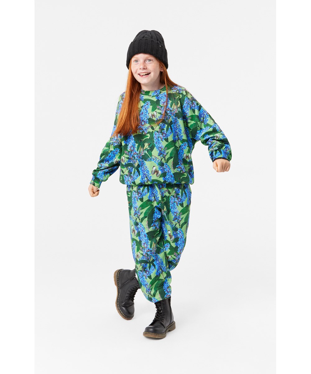 Adan - Buddleja Garden - Weiche und warme grüne Jogginghose aus Öko-Baumwolle mit einem all-over Schmetterlingsmuster.