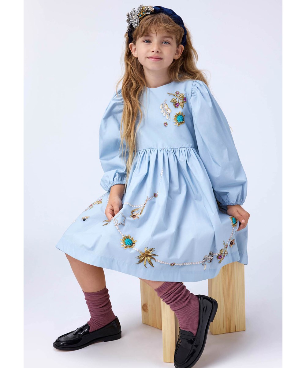 Cilja - Broches - Knielanges hellblaues Kleid für Kinder aus Öko-Baumwollpopeline mit einem Schmuckmuster.