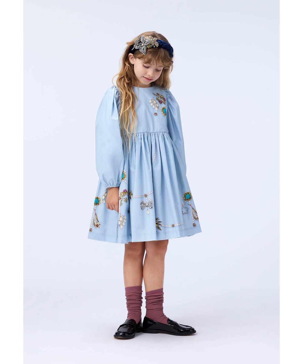 Cilja - Broches - Knielanges hellblaues Kleid für Kinder aus Öko-Baumwollpopeline mit einem Schmuckmuster.