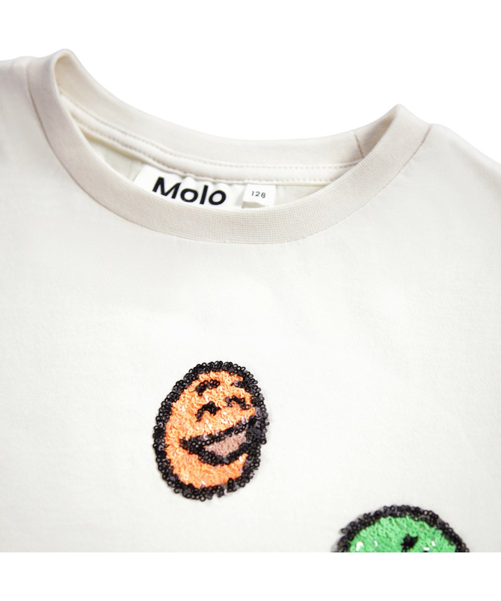 Ranva - Buttercream - Off-White T-Shirt für Kinder aus Öko-Baumwolle mit kurzen Ärmeln, Rundhalsausschnitt und lächelnden Pailletten-Gesichtern.