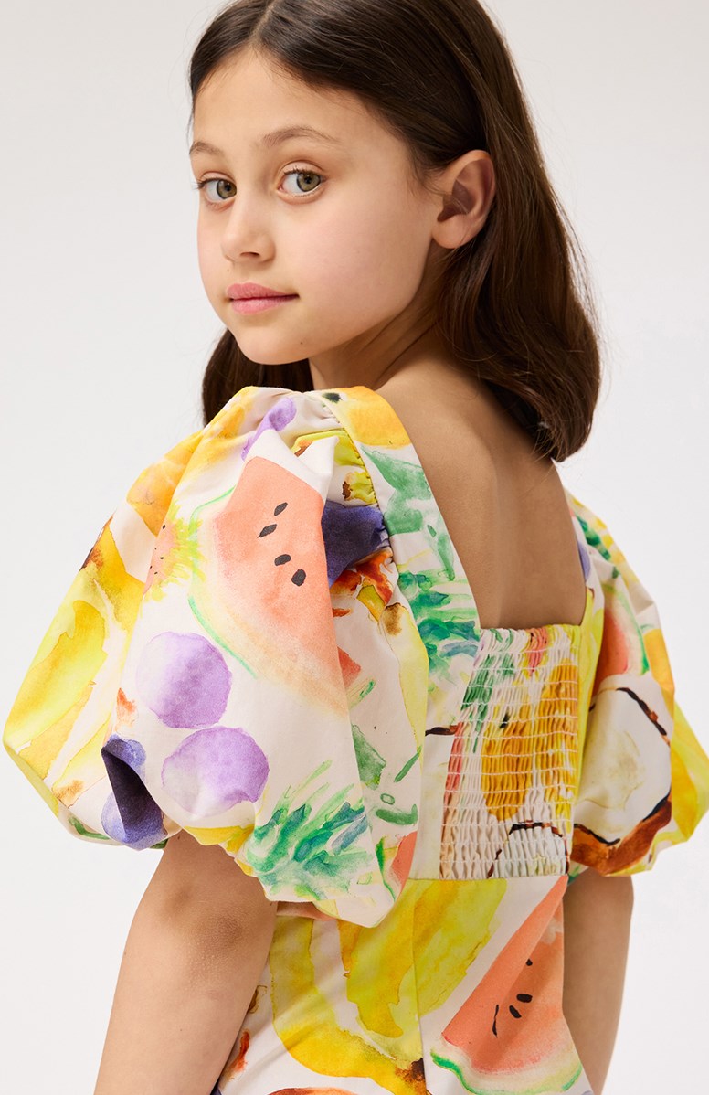 Cissy - Fruit Salad - Beige kinderjurk van biologisch katoen met pofmouwen en kleurrijke print van exotisch fruit.