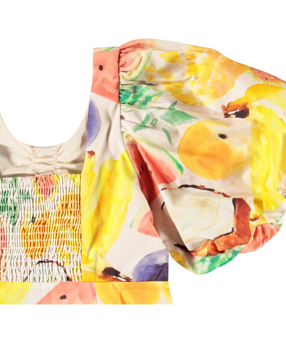Cissy - Fruit Salad - Beige kinderjurk van biologisch katoen met pofmouwen en kleurrijke print van exotisch fruit.