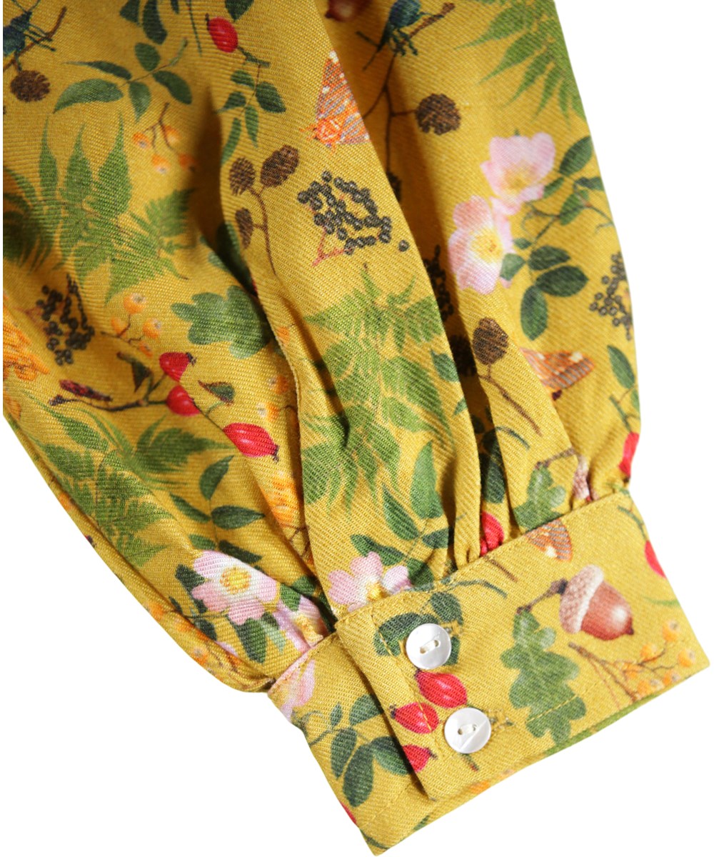 Constance - Foraging - Lange gele kinderjurk met lange mouwen met ruches en een print van bladeren, bloemen en noten.