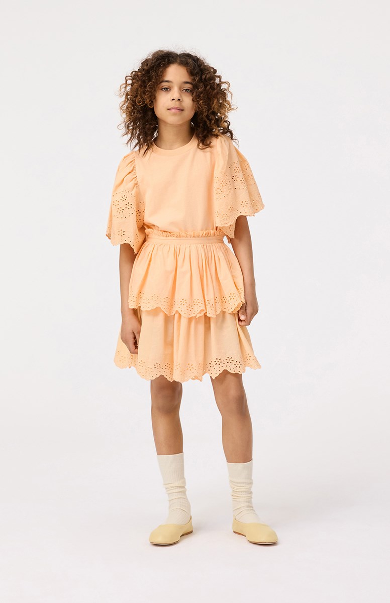 Brianna - Pale Melon - Lichtoranje kinderrok van biologisch katoen. De rok valt op de knie en heeft twee lagen in verschillende lengtes met Engels kant aan de boord.