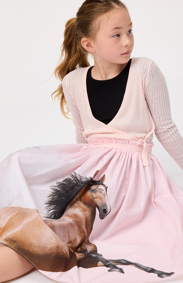 Gitte - Charlotte Pink - Roze gebreide wikkelvest voor kinderen van zacht rekbare ribpatroon De vest wordt vastgemaakt met een strik en knoop aan de zijkant.