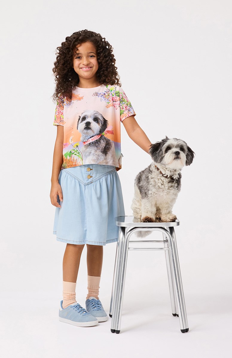 Raeesa - Festivalgoers - Lichtoranje ruimvallende kinder t-shirt in zacht biologisch katoen met een ronde hals en het is aan de achterkant langer dan aan de voorkant.