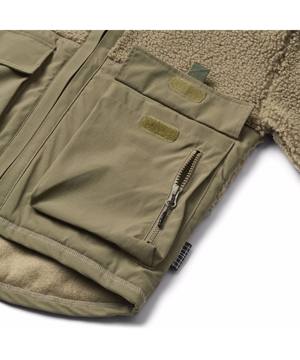 Utha - Bark Green - Dunkelgrüne Fleecejacke für Kinder aus recyceltem Polyester mit Details an den Ärmeln, am Rücken und an den äußeren Vordertaschen, die aus wind- und wasserabweisendem strapazierfähigem Nylon gefertigt sind.