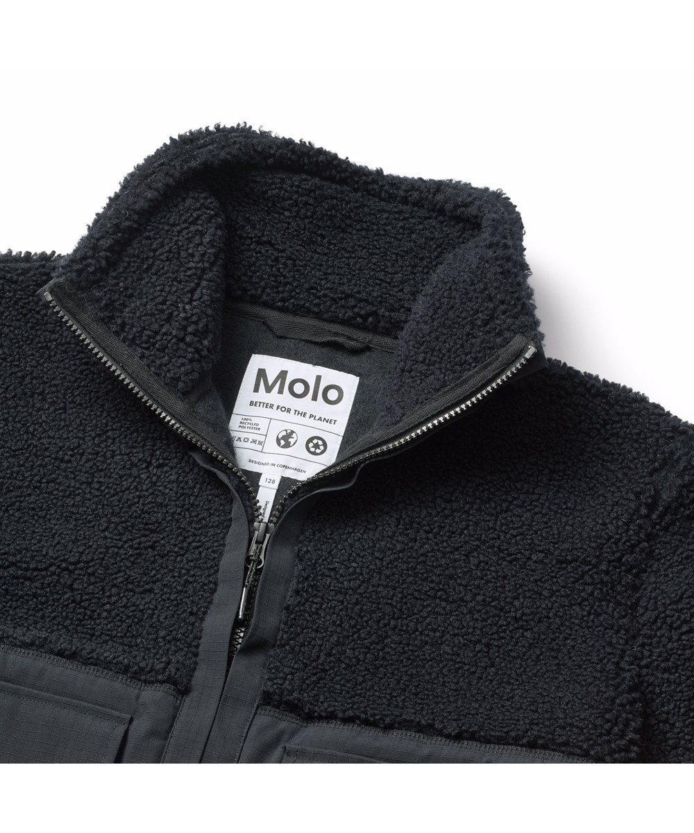 Utha - Black - Schwarze Fleecejacke für Kinder aus recyceltem Polyester mit Details an den Ärmeln, am Rücken und an den äußeren Vordertaschen, die aus wind- und wasserabweisendem strapazierfähigem Nylon gefertigt sind.