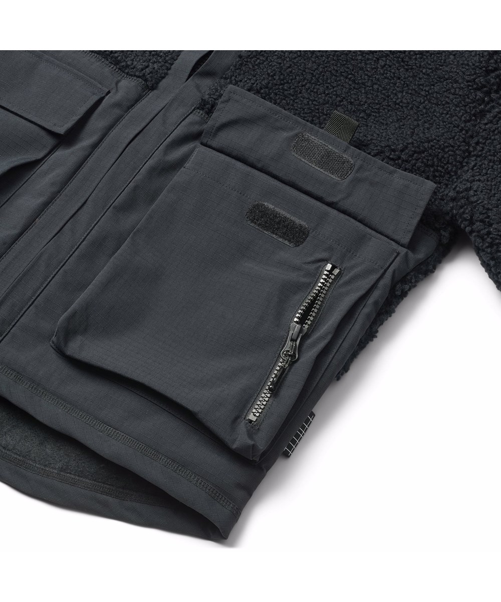 Utha - Black - Schwarze Fleecejacke für Kinder aus recyceltem Polyester mit Details an den Ärmeln, am Rücken und an den äußeren Vordertaschen, die aus wind- und wasserabweisendem strapazierfähigem Nylon gefertigt sind.