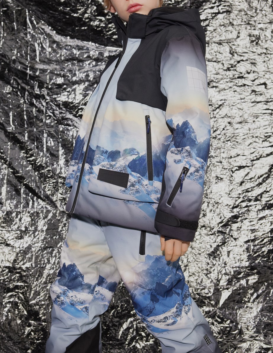 Jump Pro - High In Sky - Wind- und wasserdichte Hosen für Kinder aus recyceltem Polyester mit einem Druck von schneebedeckten Alpen mit Sonnenstrahlen und einem klaren blauen Himmel.
