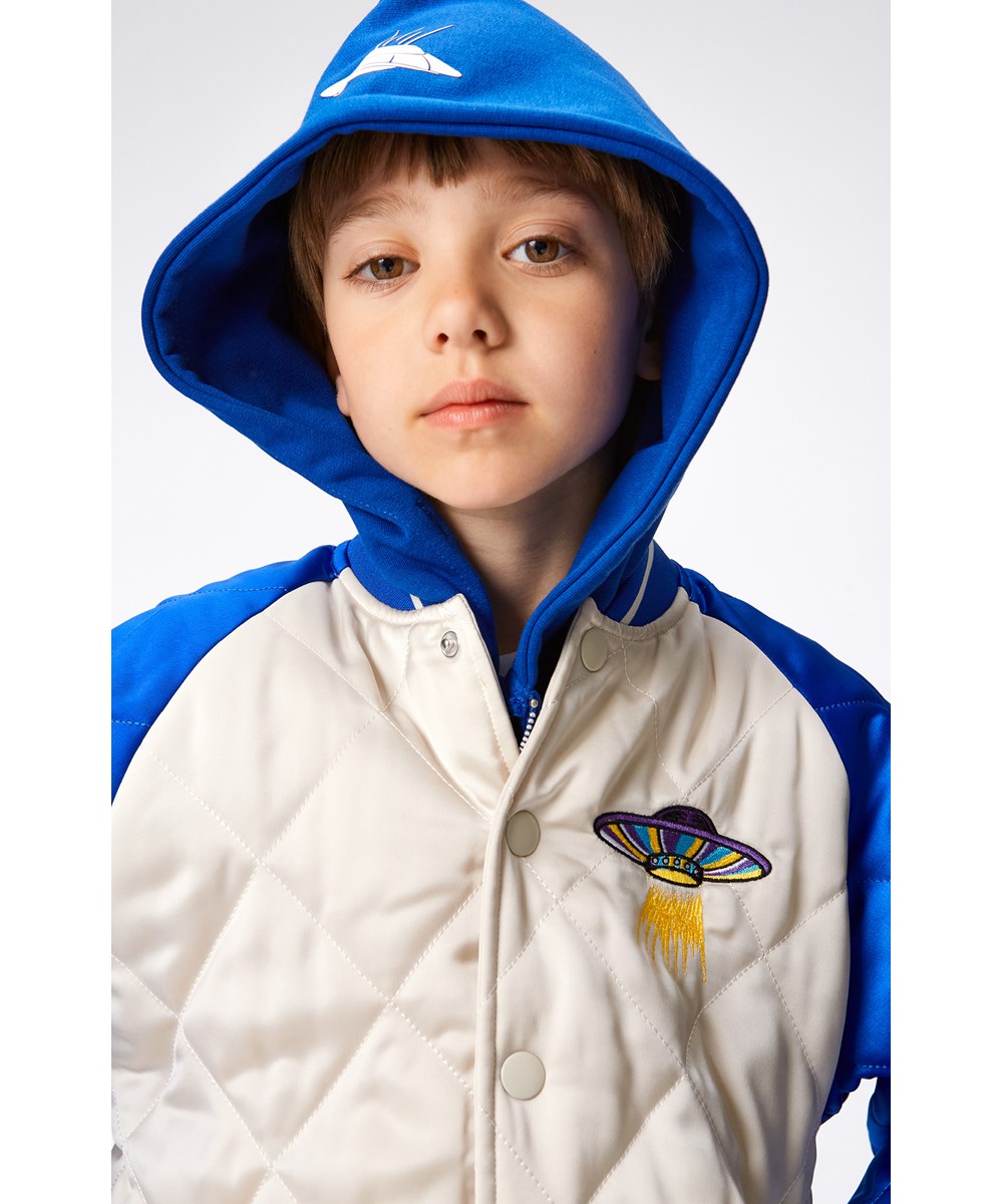 Haru - Summer Sand - Gesteppte Bomberjacke in Blau und Cremeweiß mit großem gesticktem Rückenaufnäher mit UFO, Dinosaurier und Feuer