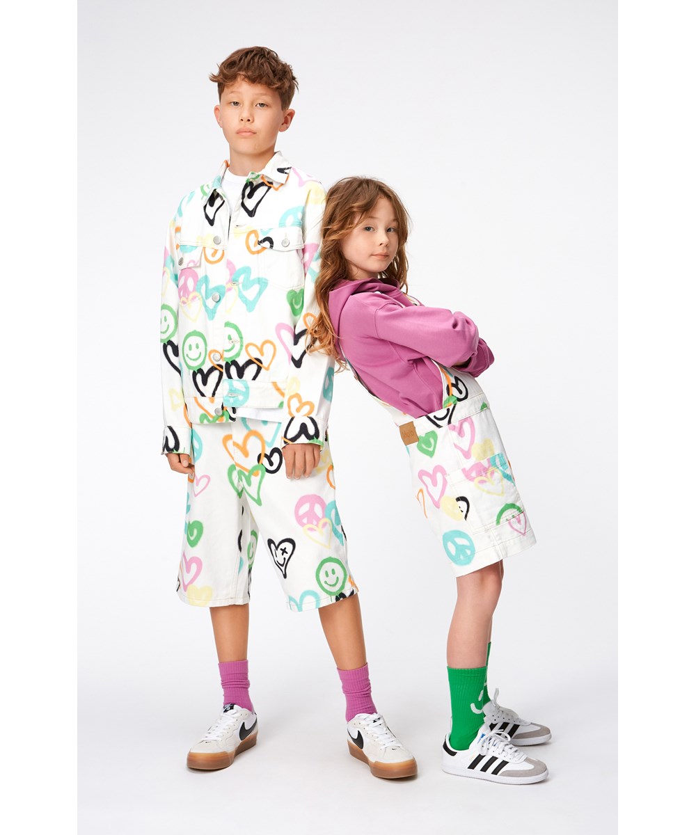 Hedly - Heart Colours - Weiße Jeansjacke für Kinder mit einem Aufdruck aus mit Graffiti bemalten Smileys, Herzen und Peace-Zeichen.