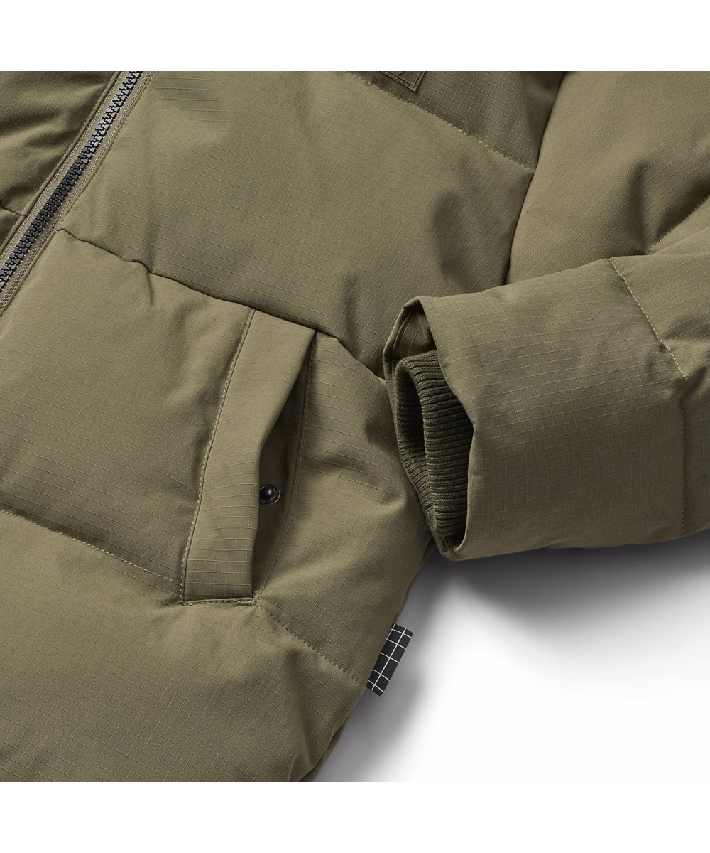 Hilo - Bark Green - Warme und funktionale dunkelgrüne Jacke für Kinder aus recyceltem Polyester mit praktischem Reißverschluss, hohem Kragen und abnehmbarer Kapuze.