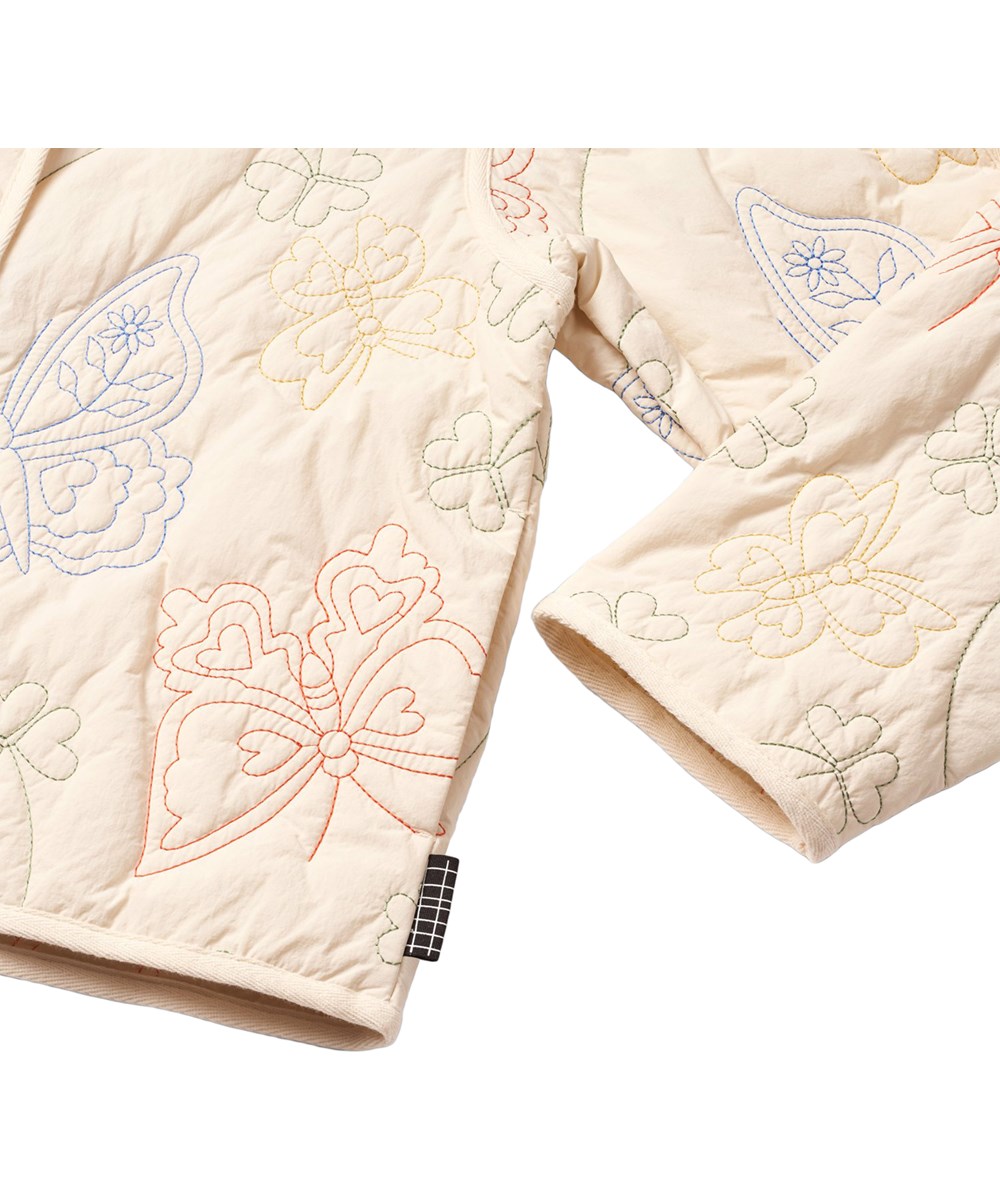 Holley - Pearled Ivory - Gesteppte Jacke für Kinder in einem hellen, cremefarbenen Ton mit gestickten Motiven von Schmetterlingen und Blumen.