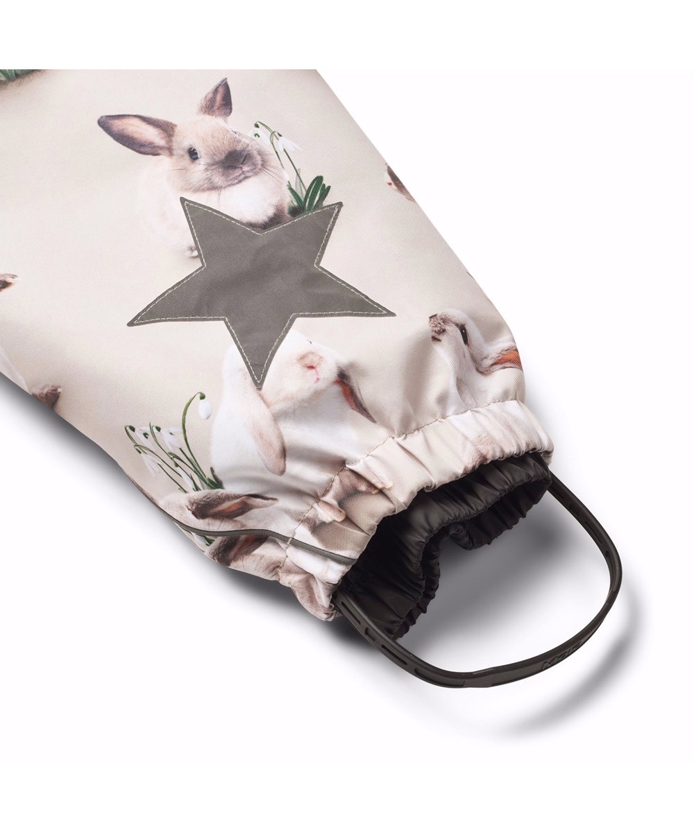 Polaris Fur - Winter Rabbits - Kinder-Schneeanzug aus recyceltem Polyester mit einem Druck von niedlichen Hasen zwischen Schneeglöckchen auf einem grauen Hintergrund.
