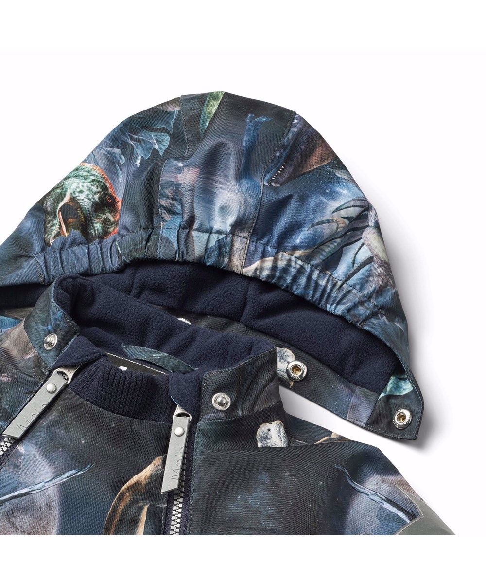 Pyxis - Dino In Space - Blaue Kinder-Schneeanzug aus recyceltem Polyester mit einem Druck von Dinosauriern im Weltraum.