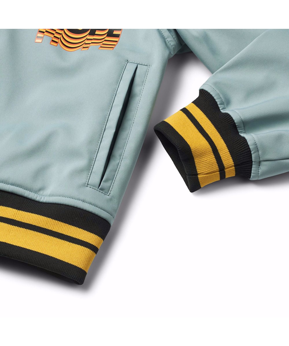 Cloudy - Misty Blue - Blue wind and water-resistant softshell jacket for children in recycled polyester, featuring small prints of positive statements and messages from the collection's themes.