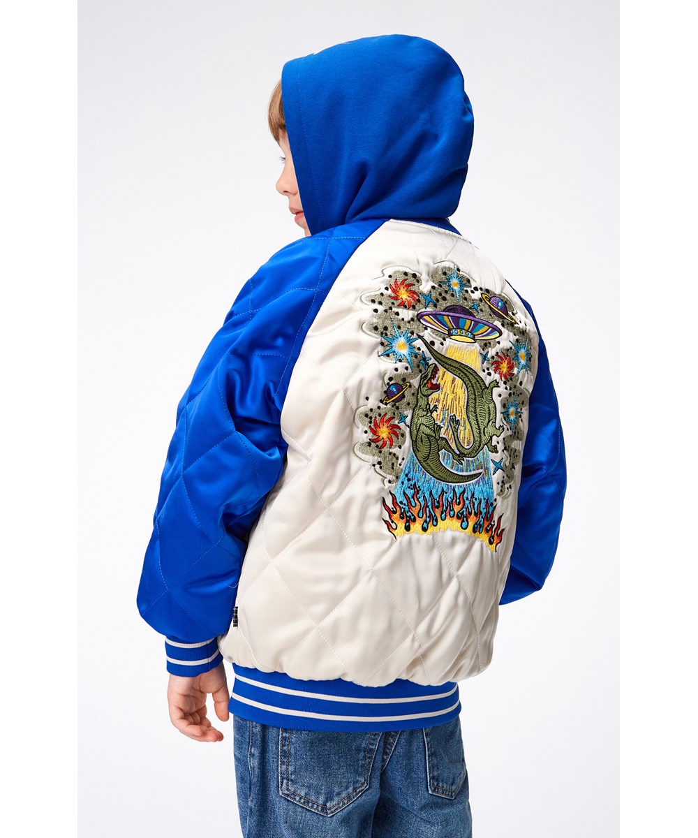 Haru - Summer Sand - Quilted bomber jacket in blue and off-white with a large embroidered patch of a UFO, a dinosaur and fire on the back