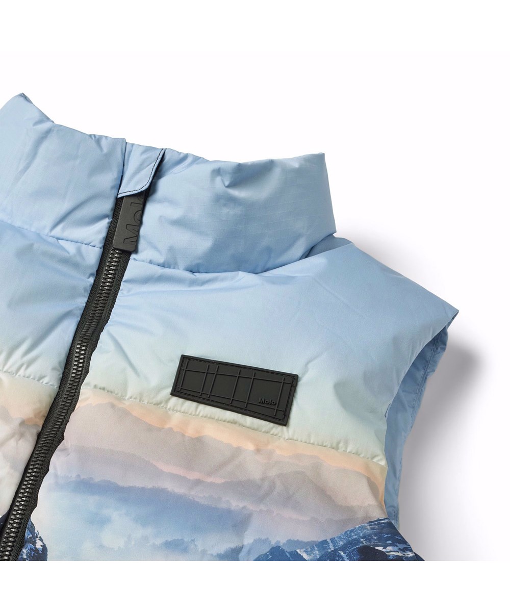Heike - High In Sky - Warm vest for children in recycled polyester with a print of snow-covered Alps, sun rays and a clear sky.