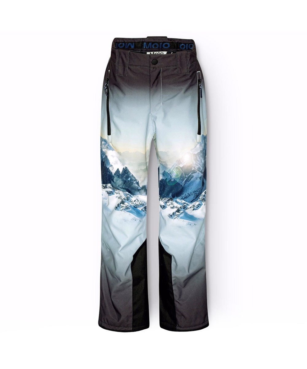 Jump Pro - High In Sky - Wind- and waterproof trousers for children in recycled polyester with a print of snow-covered Alps with sun rays and a clear blue sky.