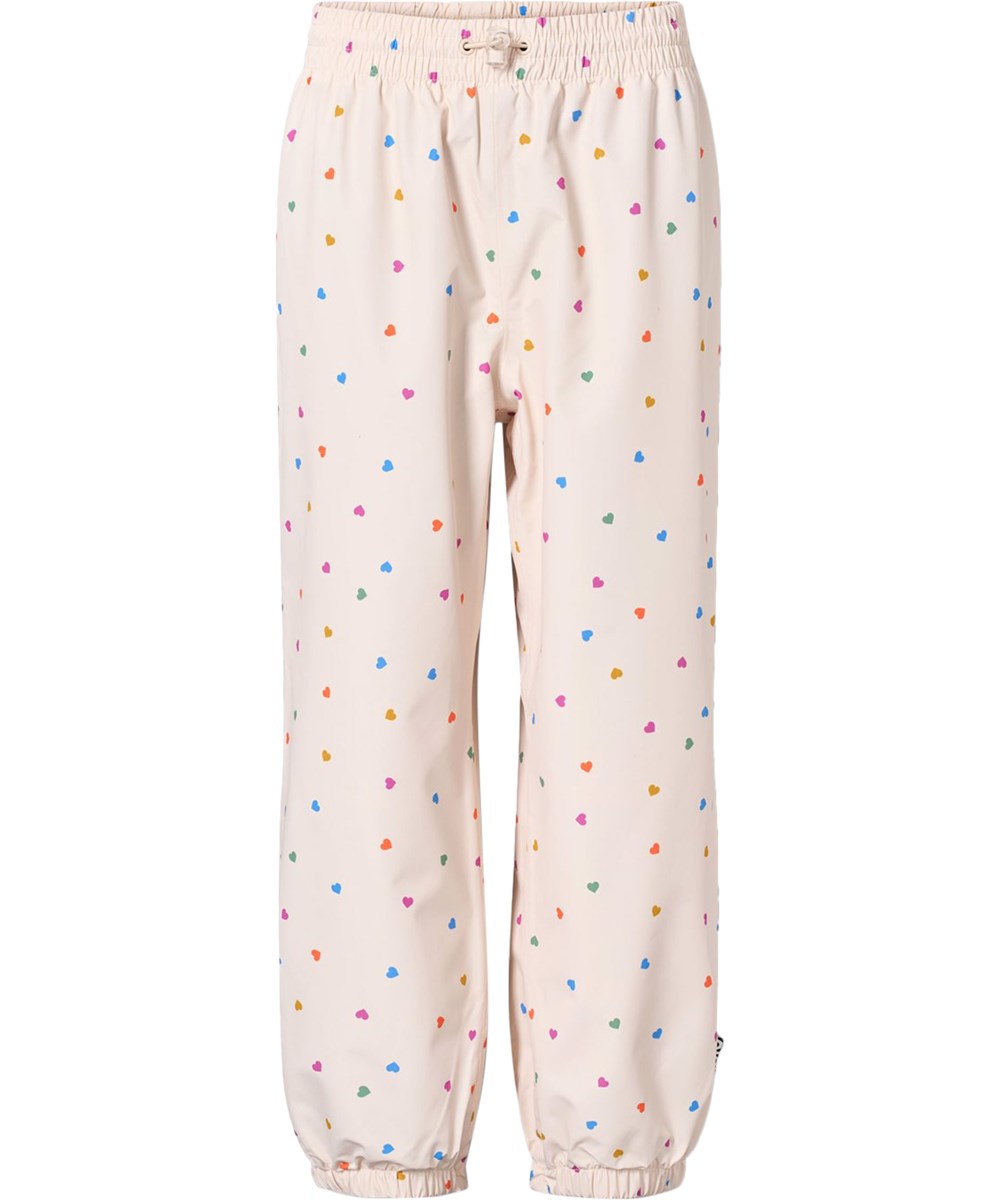 Waits - Confetti_Rainbow - Waterproof rain trousers in recycled polyester. The trousers are beige with a print of small hearts in various colours.
