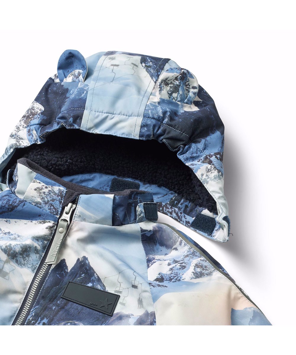 Hyde - Mountain High - Flyverdragt til en kold vinter i genanvendt polyester,  i et vinterlandskabsprint i blå nuancer. Flyverdragten har elastik i lænden, ved ærme- og ben afslutning, så sne, regn og vind holdes ude, samt holder på luffer og støvler