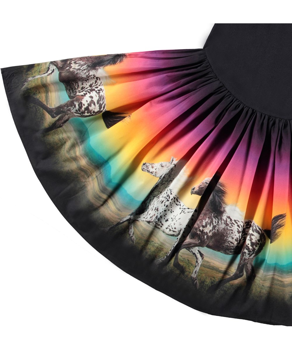Casie - Magic Sunset - Langærmet sort kjole med rundskåret skørt i økologisk bomuld med et print af galloperende heste, bjerge i baggrunden og en regnbuefarvet himmel
