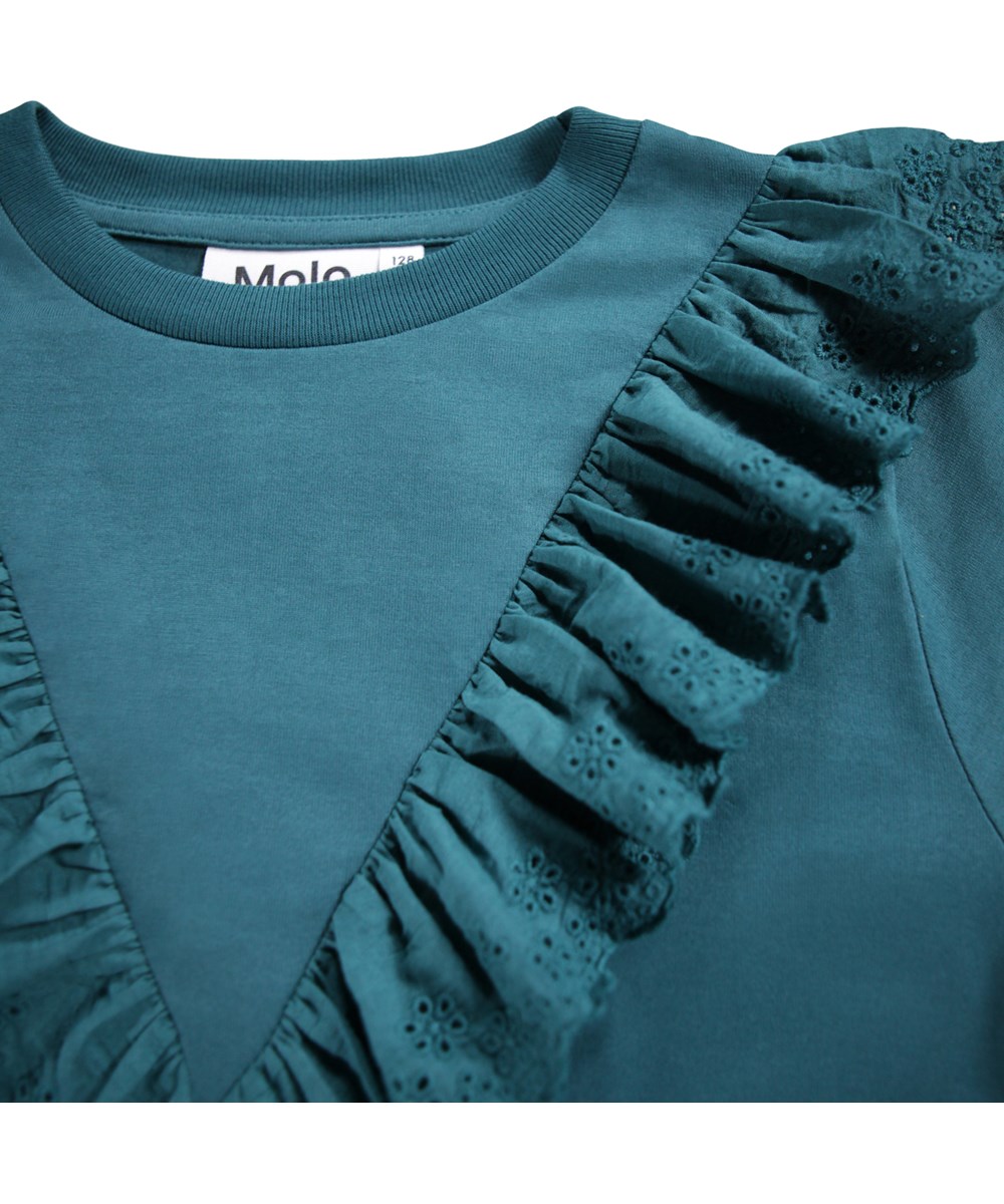 Rheta - Cosmic Green - Petroliumsgrøn, langærmet bluse til børn i økologisk bomuld med rund hals og ribkant samt en flæsekant i broderi anglaise.