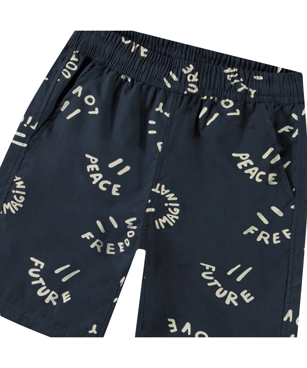 Avart - Smile Words - Knälånga shorts i ekologisk bomull för barn. Dessa shorts är blåa med leende ansikten.