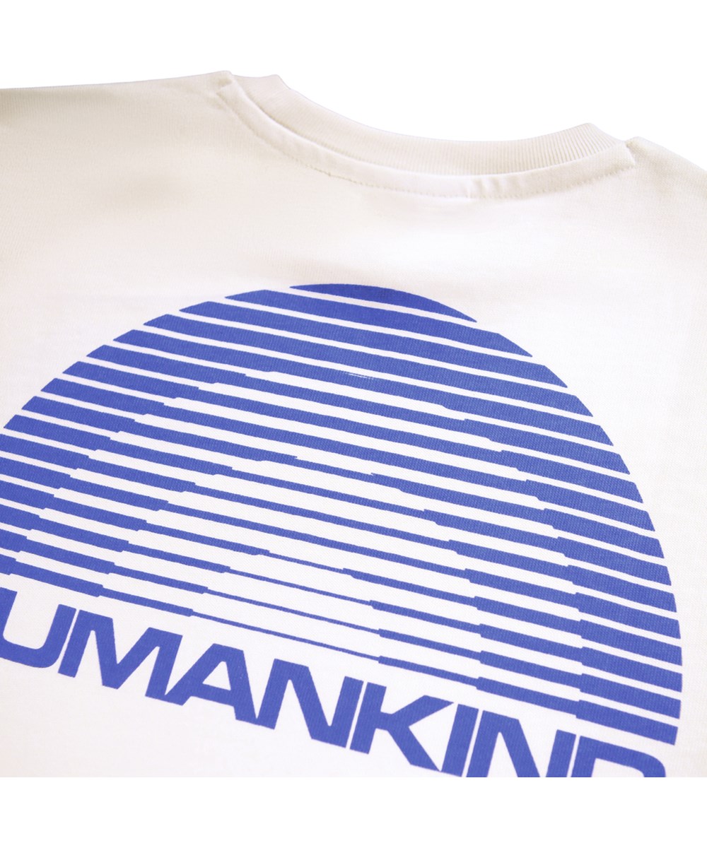 Riley - Humankind - Vit t-shirt för barn i mjuk ekologisk bomull med korta ärmar och en ribbad halsringning samt en blå regnbåge med texten ''Humankind''.