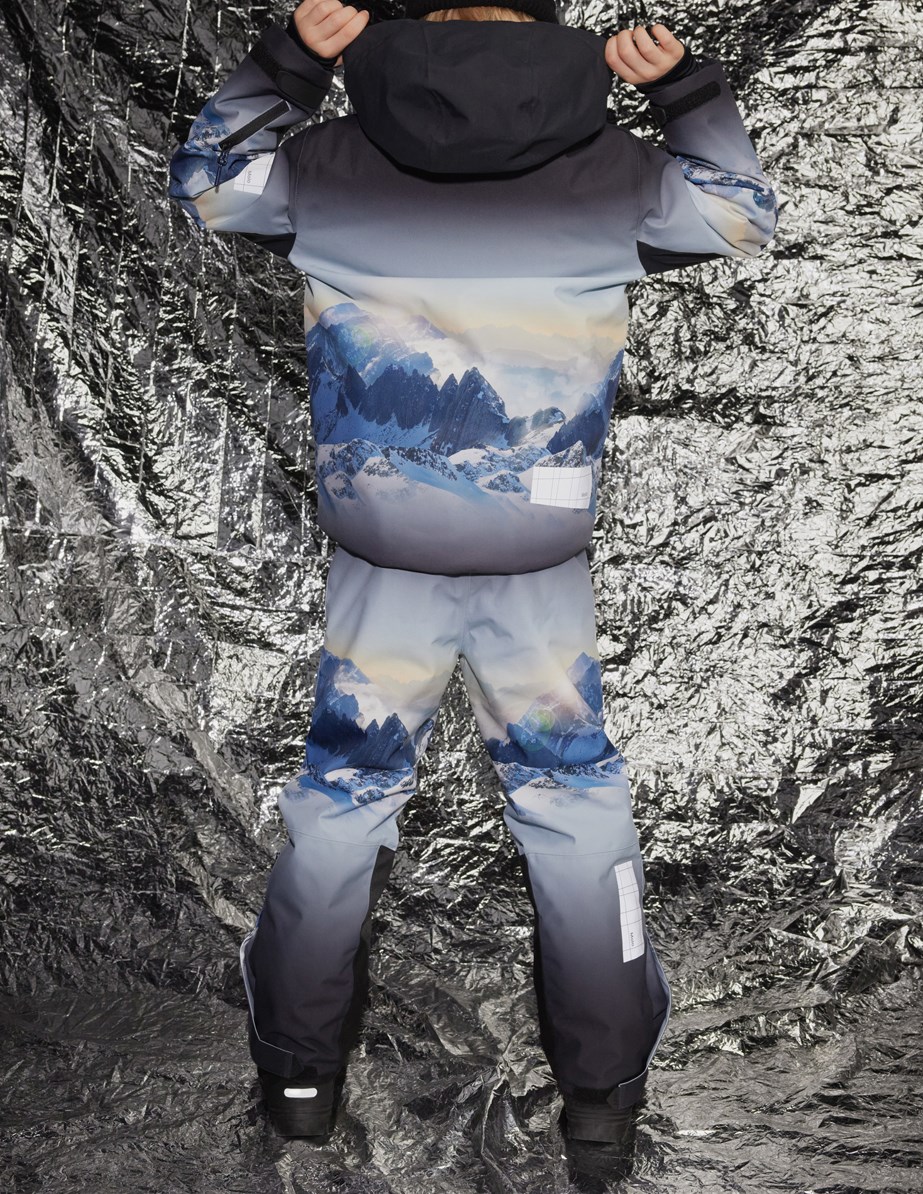 Jump Pro - High In Sky - Vind- och vattentäta byxor för barn i återvunnen polyester med ett tryck av snötäckta Alper med solstrålar och en klarblå himmel.