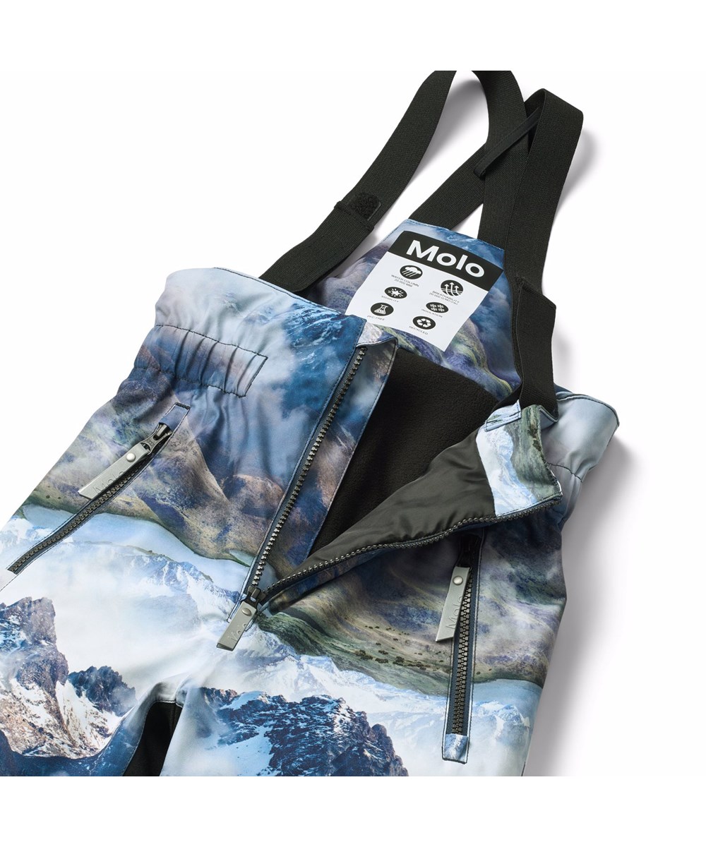 Play Pro - Snowy Mountains - Vind- och vattentäta skidbyxor tillverkade av återvunnen polyester med ett vackert landskapsmönster som visar snötäckta bergstoppar i levande färger. Skidbyxorna har justerbara hängslen och är vadderade med 3M™ Thinsulate™.