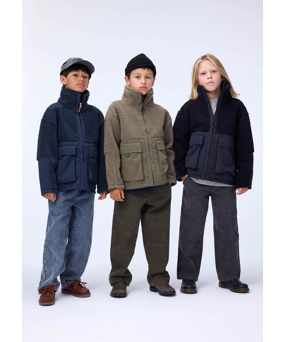 Utha - Bark Green - Mörkgrön fleecejacka för barn tillverkad av återvunnen polyester med detaljer på ärmarna, baksidan och yttre framfickor som är gjorda av vind- och vattenavvisande slitstark nylon.