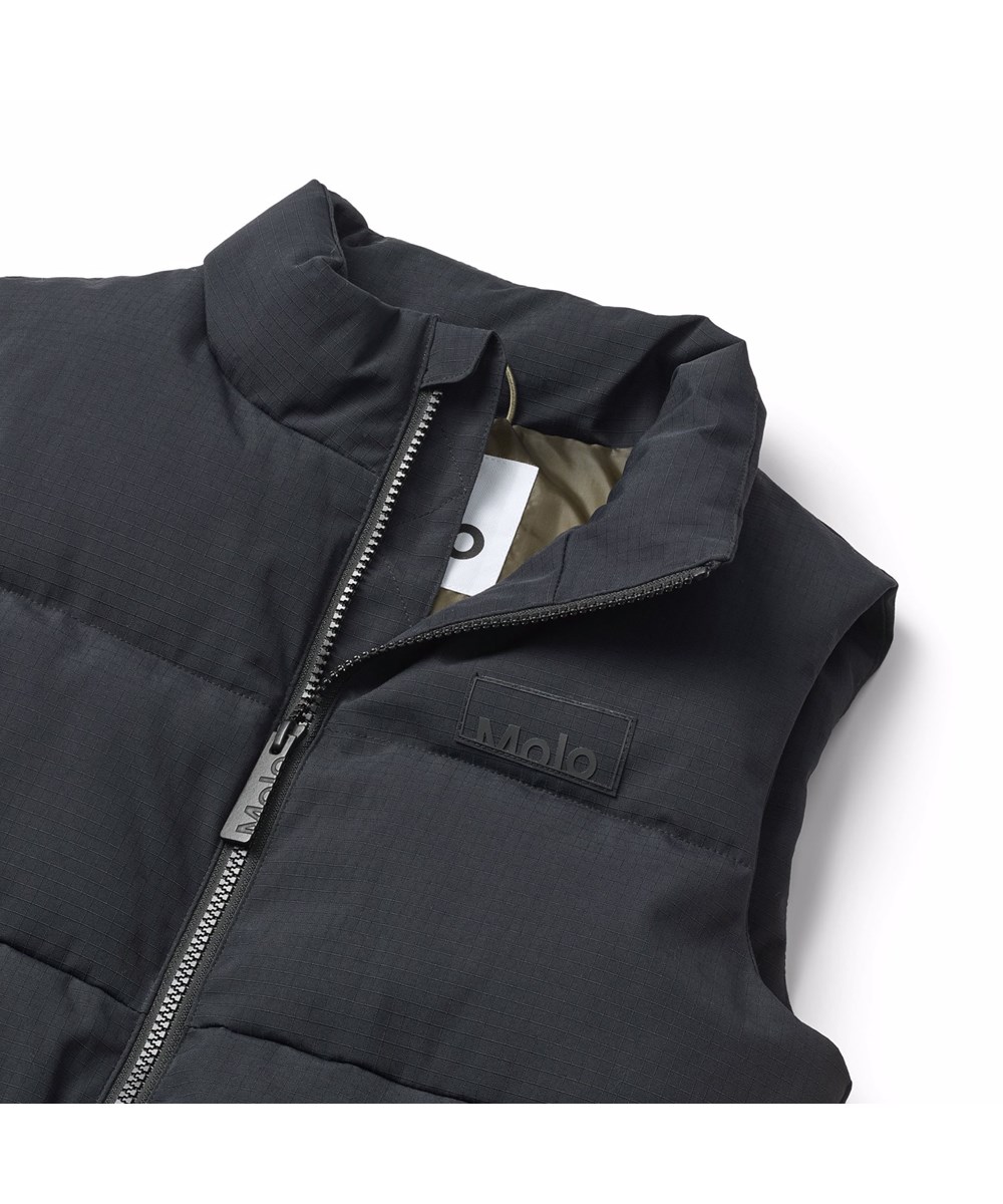 Heike - Black - Svart vadderad väst för barn i återvunnen nylon med dragkedja framtill, hög krage och stora ärmhål, vilket gör det möjligt att bära en jacka eller tjock tröja under.