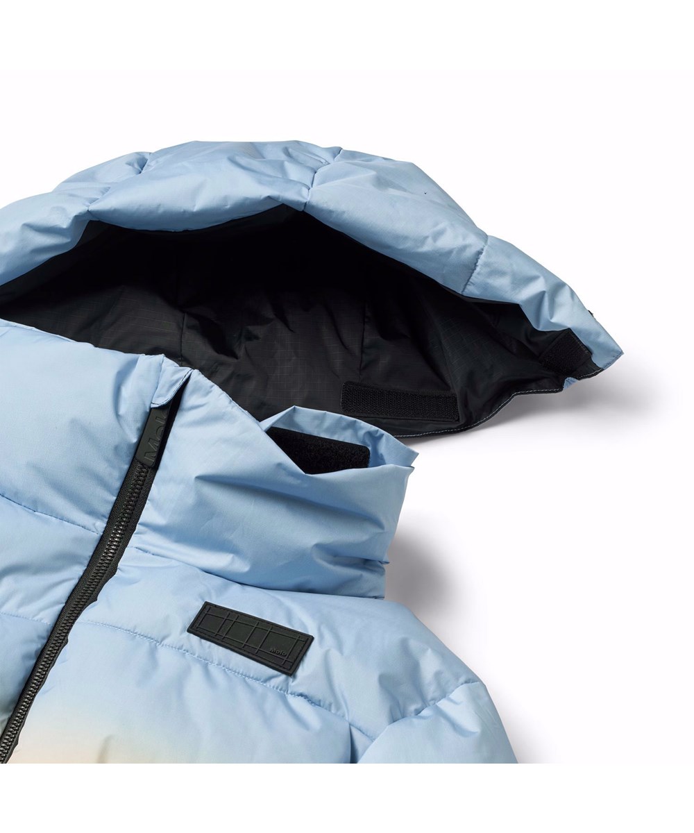 Hilo - High In Sky - Varm dunjacka för barn i återvunnen polyester med ett tryck av snöklädda alper med solstrålar och en klarblå himmel.