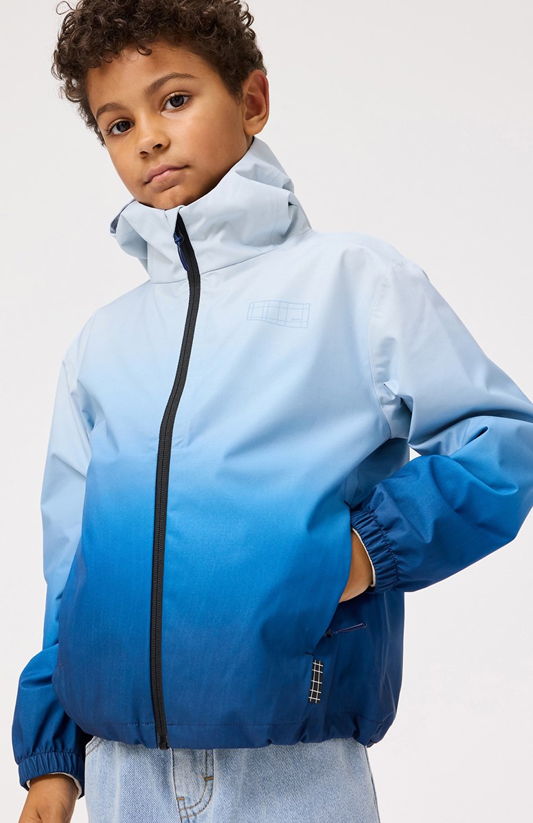Horizon - Fade Blue - Vind- och vattentät jacka för barn i återvunnen polyester med en huva i blåa gradientfärger.